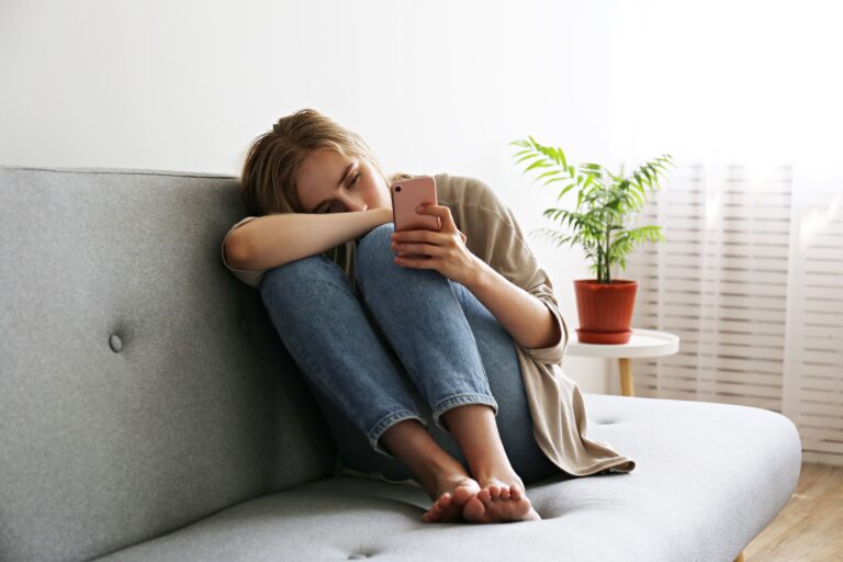 femme assise sur un canapé regardant son téléphone