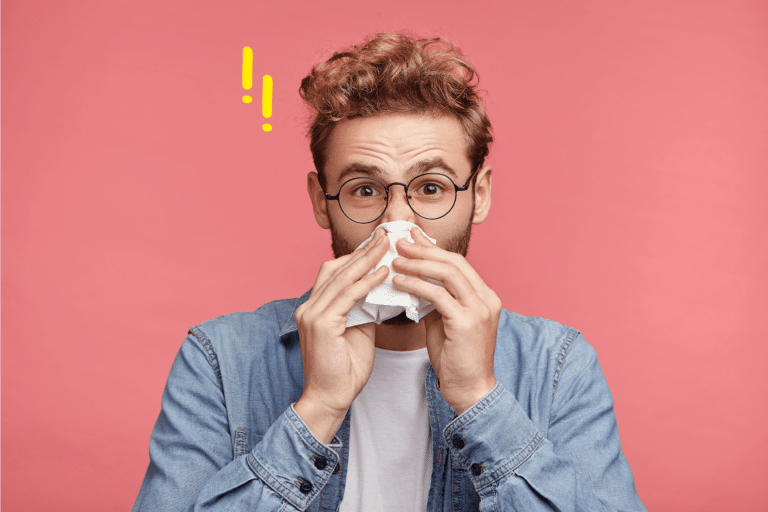 Homme avec des lunettes se mouchant, sur fond rose