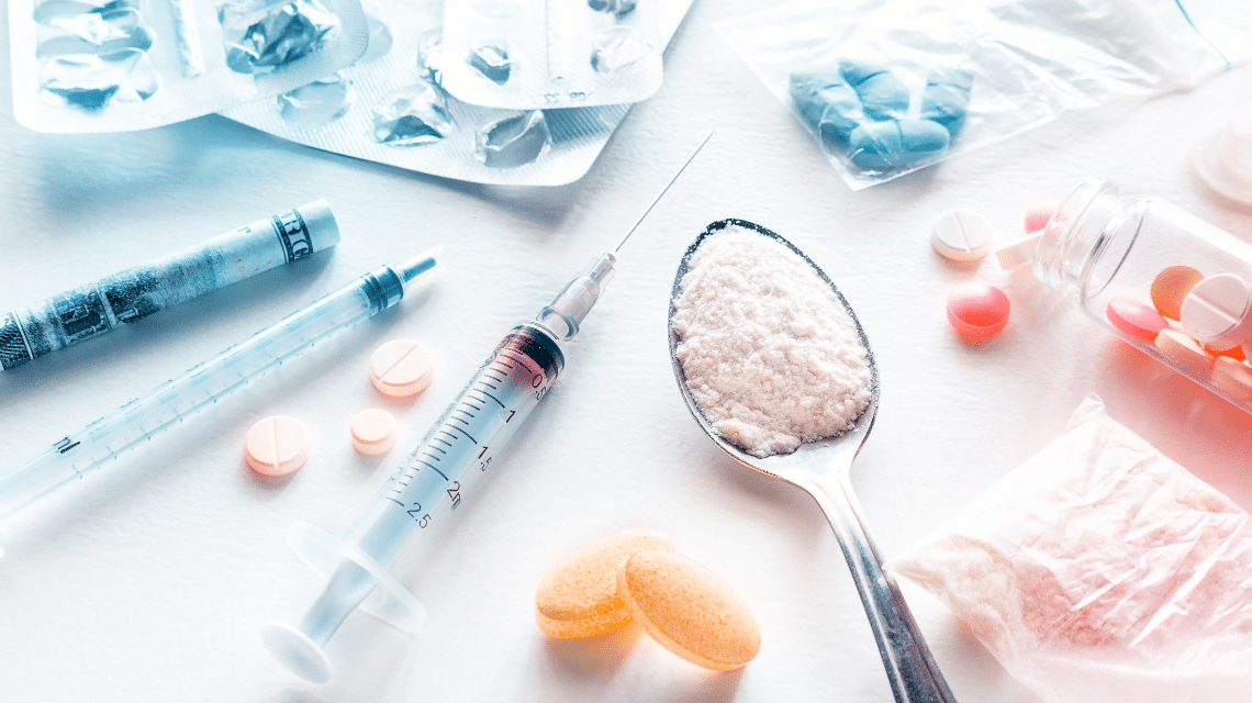 Différents types de drogues et accessoires de consommation, incluant des comprimés, de la poudre blanche, des seringues et des sachets, posés sur une table.