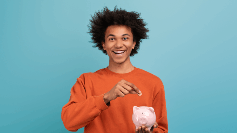 Un jeune étudiant souriant, vêtu d’un sweat orange, met une pièce dans une tirelire rose en forme de cochon sur fond bleu clair.