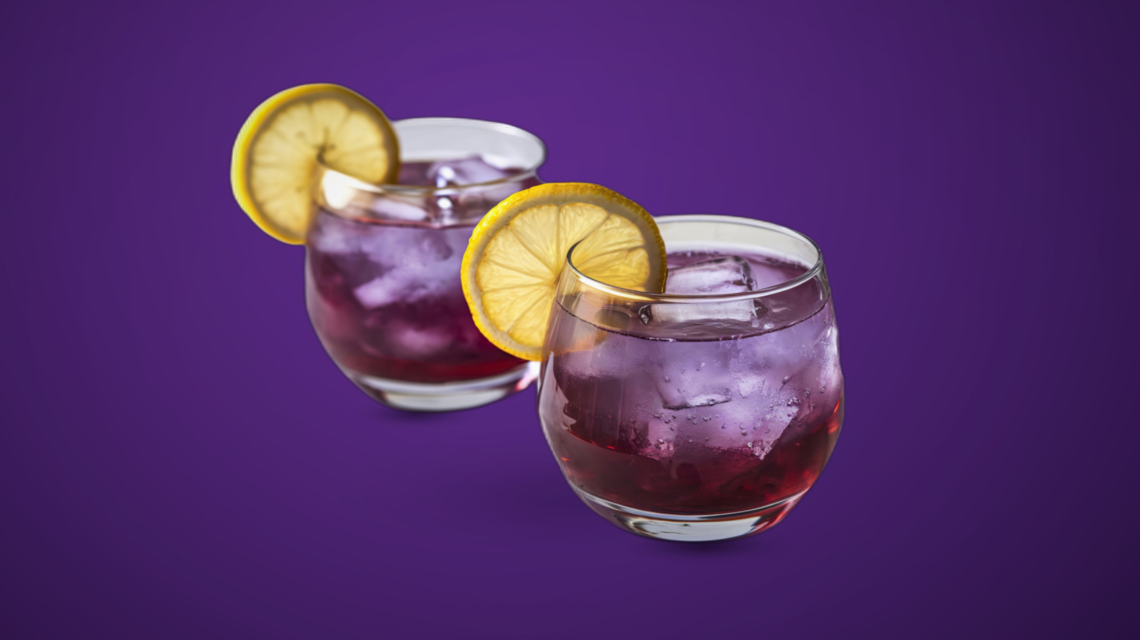Deux verres de cocktail violet garnis de citron sur fond violet foncé, illustration de l'article LMDE sur les dangers de la Lean